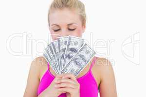 Woman holding fanned banknotes in front of face with eyes closed