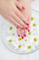 Red painted finger nails and bowl of flowers