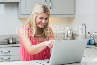 Happy young woman using laptop in kitchen