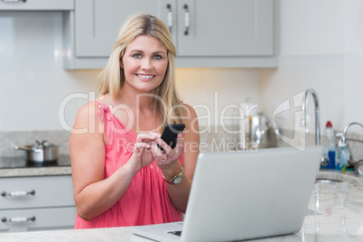 Woman text messaging while using laptop in the kitchen