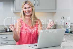 Excited woman with clenched fists using laptop in the kitchen