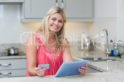 Woman holding credit card and digital tablet in kitchen