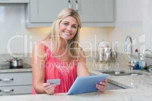 Woman holding credit card and digital tablet in kitchen