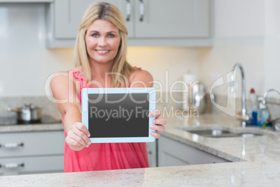 Portrait of casual woman holding out digital tablet in kitchen