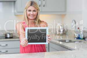 Portrait of casual woman holding out digital tablet in kitchen