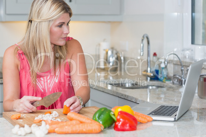 Woman cooking whilst looking at laptop