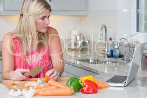 Woman cooking whilst looking at laptop