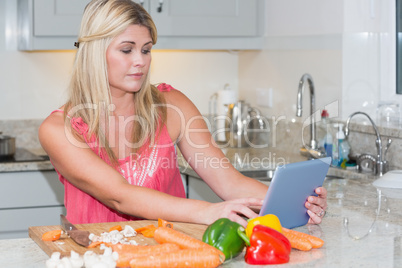 Woman cooking whilst looking at digital tablet in kitchen