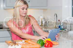 Woman cooking whilst looking at digital tablet in kitchen