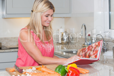 Woman reading cookbook book while cutting vegetables in kitchen