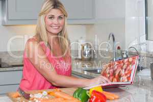 Portrait of woman reading cookbook book while cutting vegetables