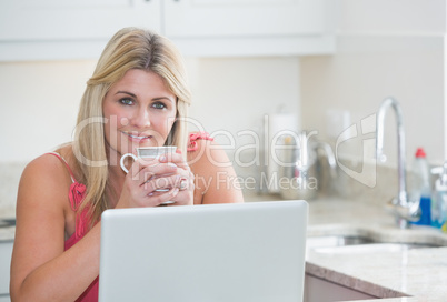 Woman with coffee cup and laptop in the kitchen