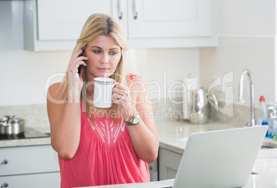 Woman with laptop and coffee cup on call in kitchen
