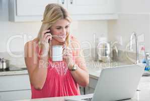 Happy woman with laptop and coffee cup on call in kitchen