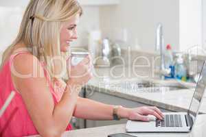 Casual woman with coffee cup using laptop in the kitchen