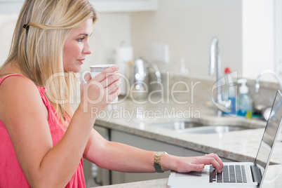 Casual woman with coffee cup using laptop in the kitchen