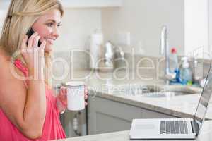 Happy woman with laptop and coffee cup on call in the kitchen