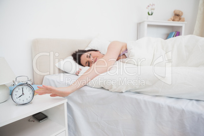 Sleepy woman extending hand to alarm clock