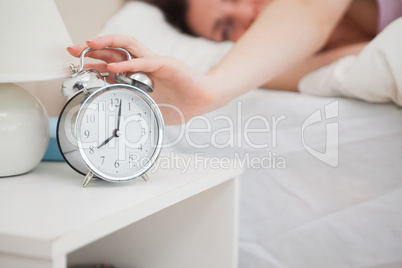 Sleepy woman in bed extending hand to alarm clock