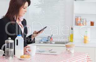 Business woman text messaging while having breakfast in kitchen
