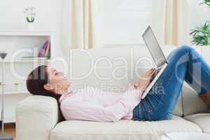 Happy woman lying on sofa and using laptop