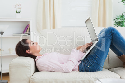 Casual woman lying on sofa and using laptop