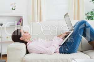 Casual woman lying on sofa and using laptop