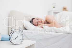 Woman sleeping in bed with focus on alarm clock