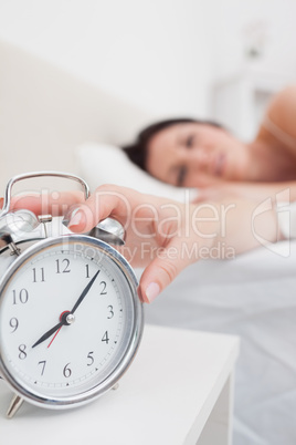 Woman in bed extending hand to alarm clock