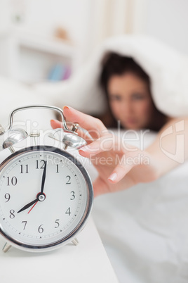 Woman in bed extending hand to alarm clock