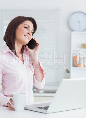 Woman with coffee and laptop using cellphone