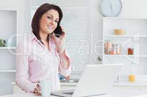 Woman with coffee cup and laptop using cellphone