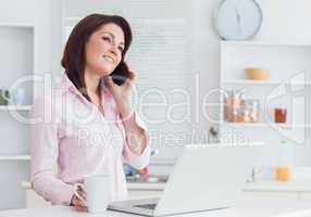 Woman with coffee cup and laptop using cellphone