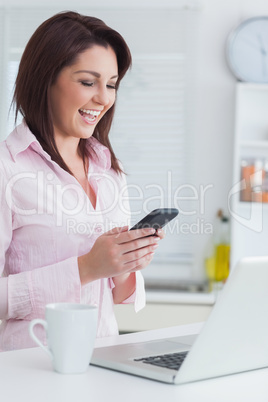 Cheerful woman reads text message while using laptop