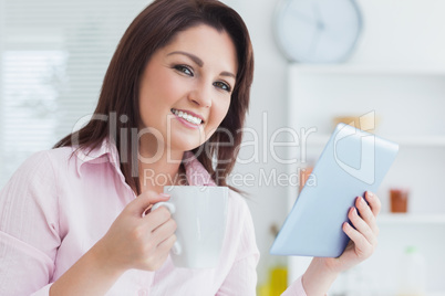 Close-up of smiling woman with coffee cup and digital tablet