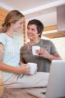 Couple looking at each with coffee cups while using laptop