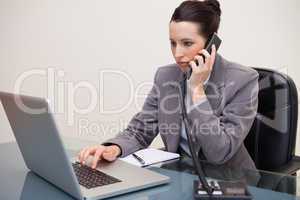Business woman using laptop while on call