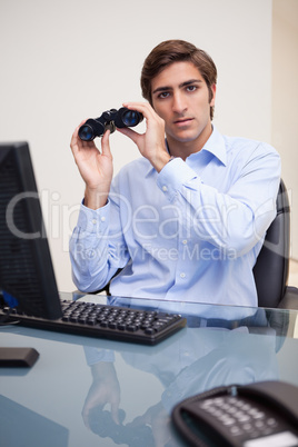 Business man with binoculars sitting at office desk