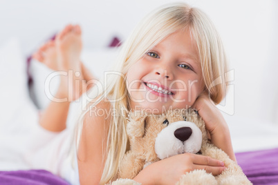 Little girl with her teddy bear lying on a bed