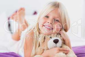 Little girl with her teddy bear lying on a bed