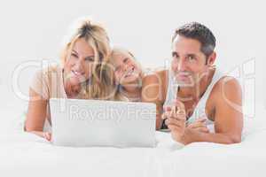 Family lying on a bed with laptop