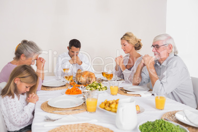 Family saying grace before eating a turkey