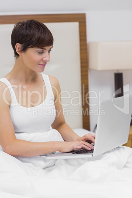 Smiling woman using laptop in bed