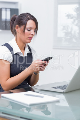 Business woman text messaging in front of laptop at office