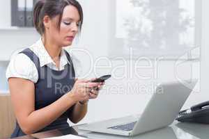 Business woman text messaging in front of laptop