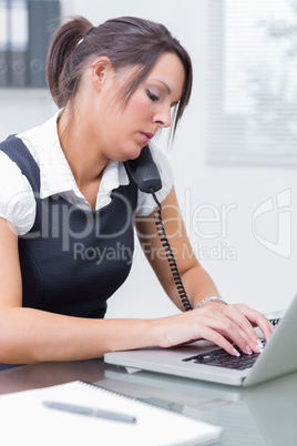 Female executive using laptop and phone at desk