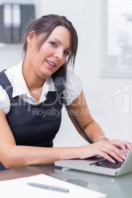 Business woman using landline phone and laptop at desk