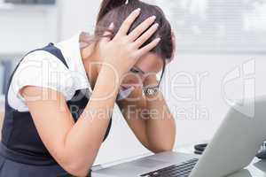 Frustrated business woman with head in hands in front of laptop