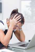 Frustrated business woman with head in hands in front of laptop