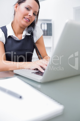 Business woman using landline phone and laptop